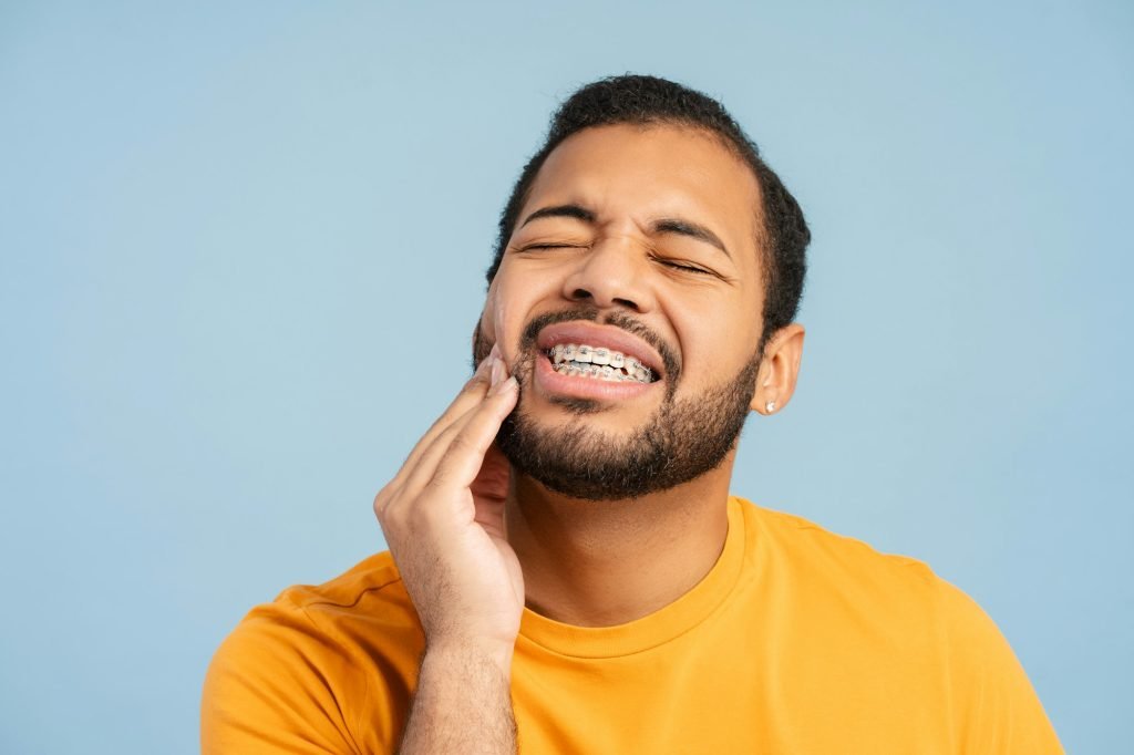 Portrait of troubled, african american man with braces, holding his cheek in pain