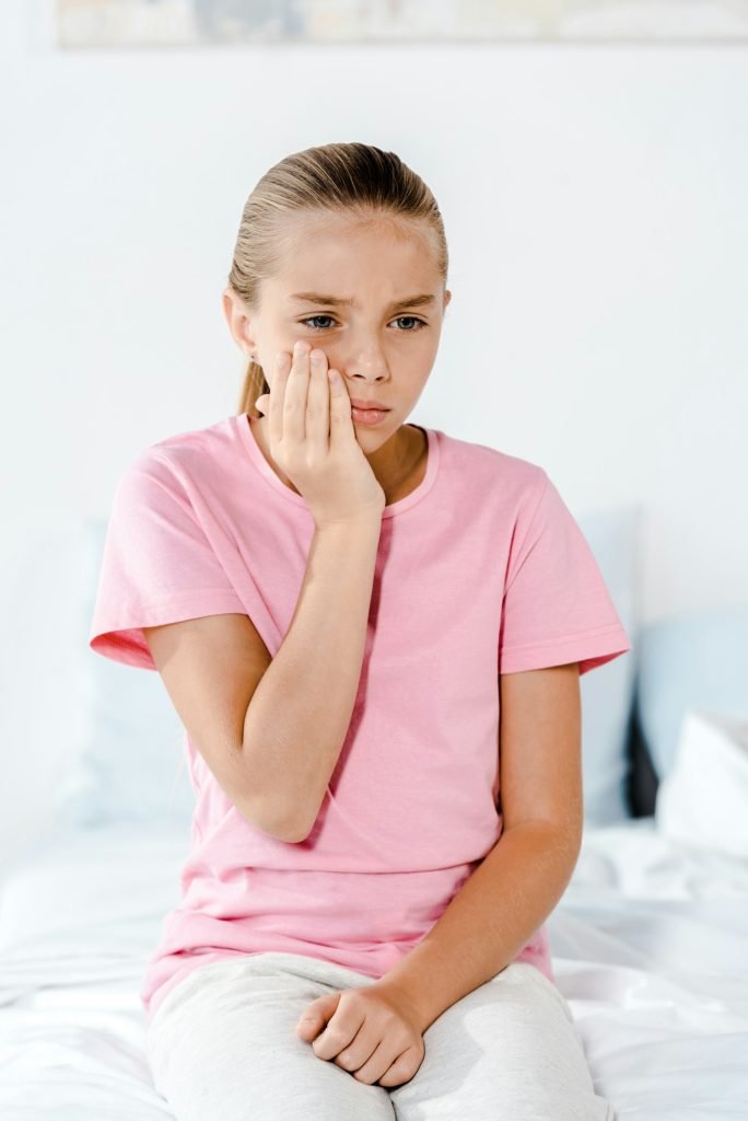 upset kid touching cheek while having tooth ache