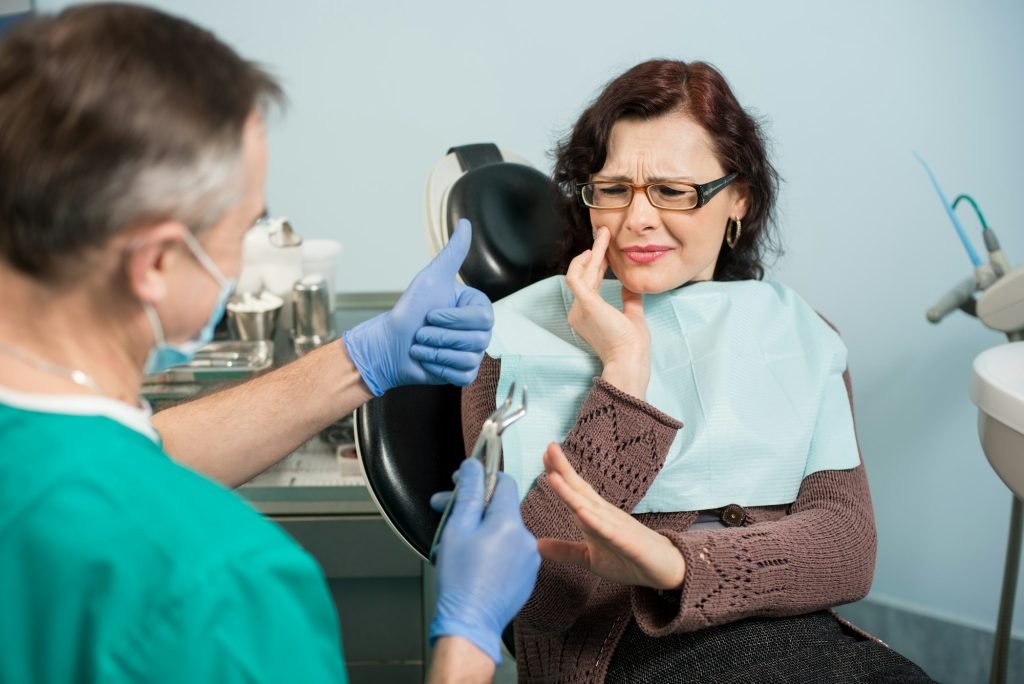 Woman feeling toothache, touching cheek with hand at dental clinic.